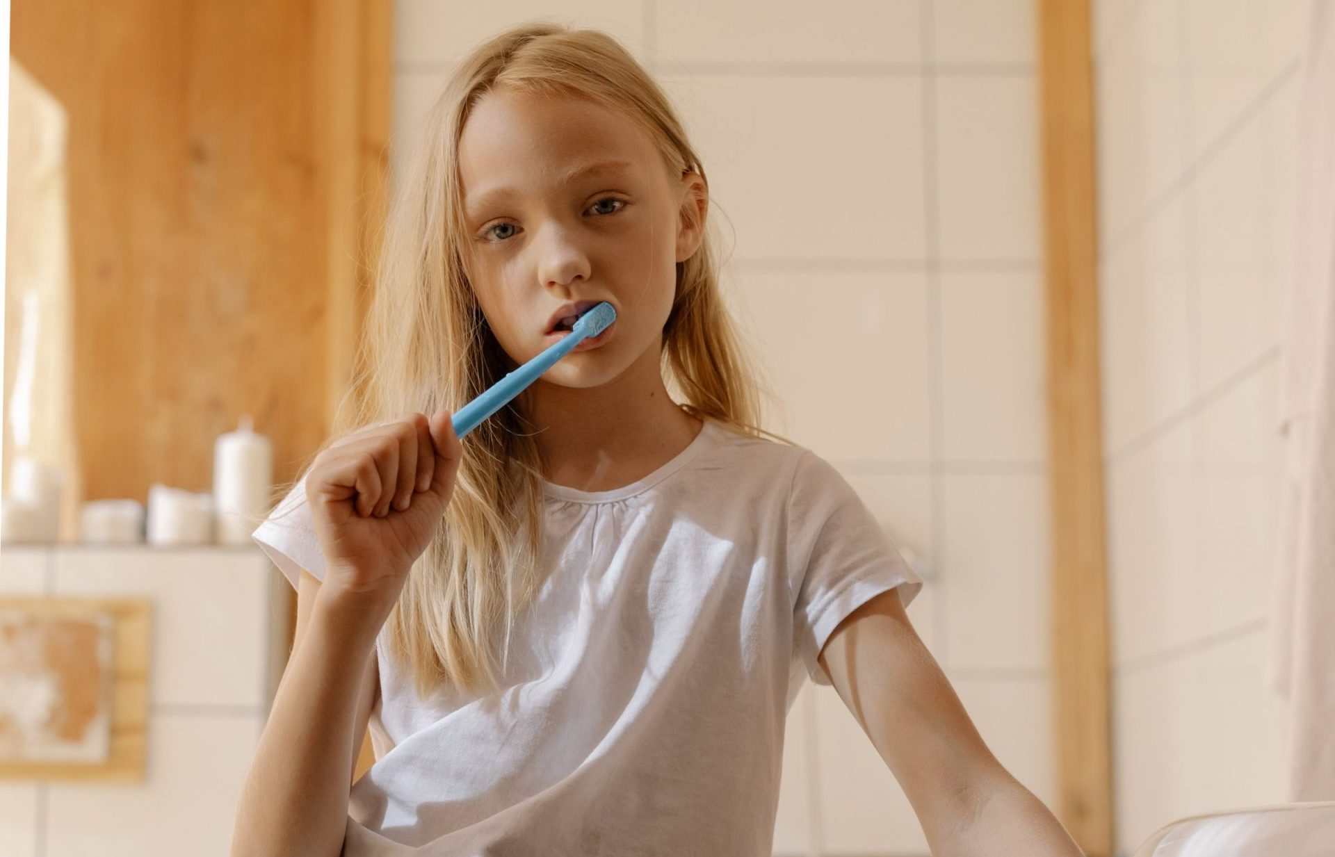 Little girl brushing her teeth with a blue toothbrush