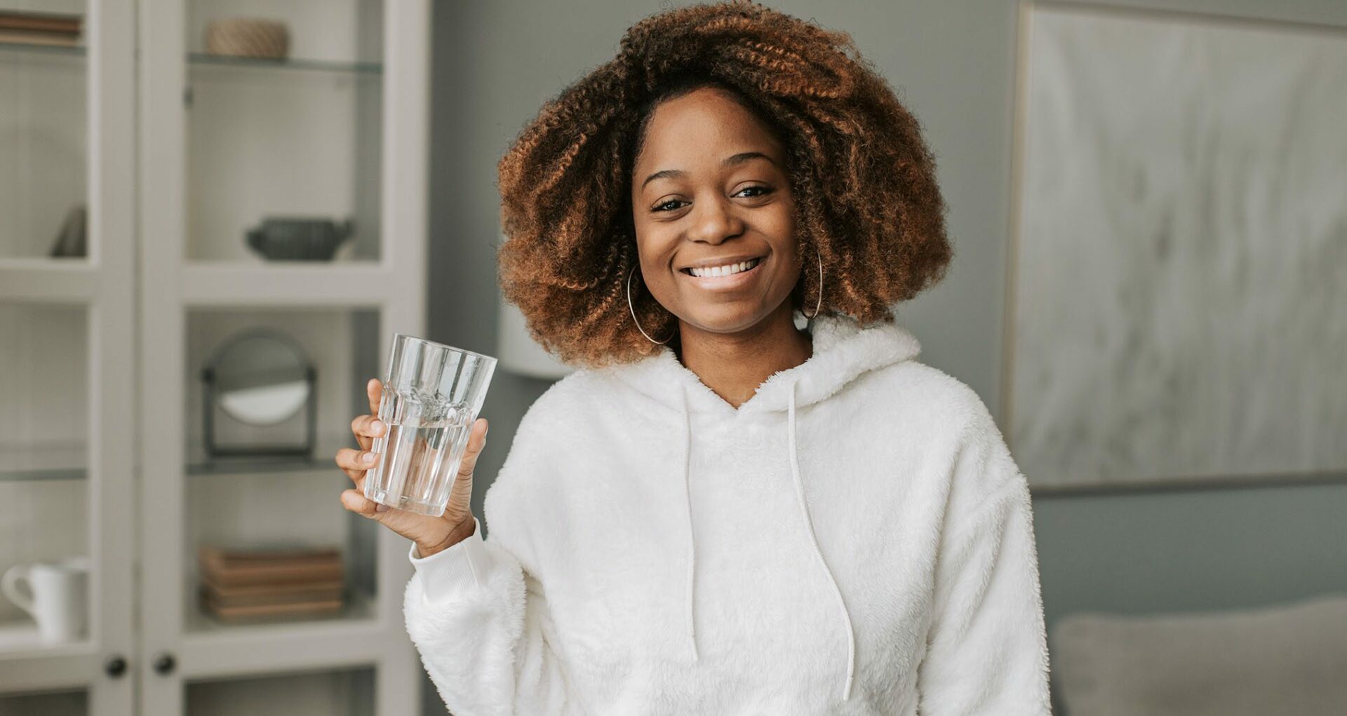 woman in hoodie drinking a fresh glass of water