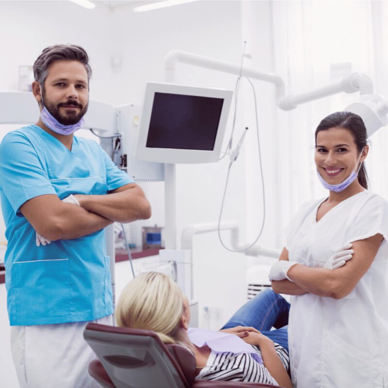male and female dentist standing in clinic with patient in chair male and female dentist standing in clinic with patient in chair