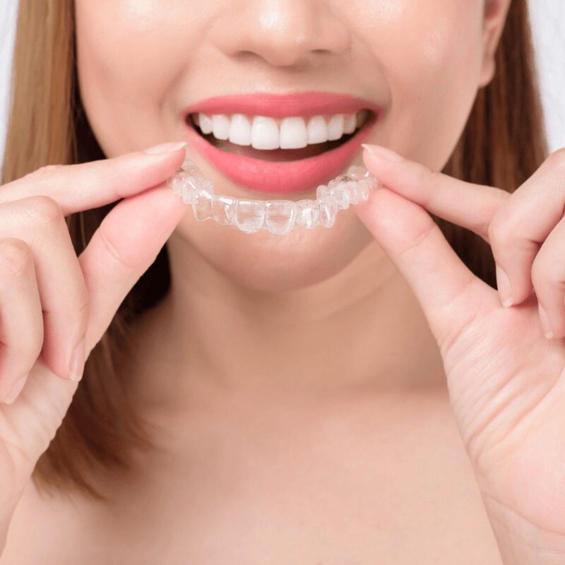 smiling-woman-holding-invisalign-braces woman smiling putting on invisalignb braces