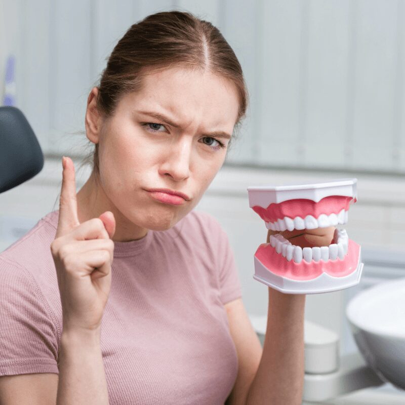 adult woman holding toy teeth gesturing to have dental cleanings done regularly adult woman holding toy teeth gesturing to have dental cleanings done regularly