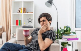 young man experiencing tooth pain at home while drinking coffee