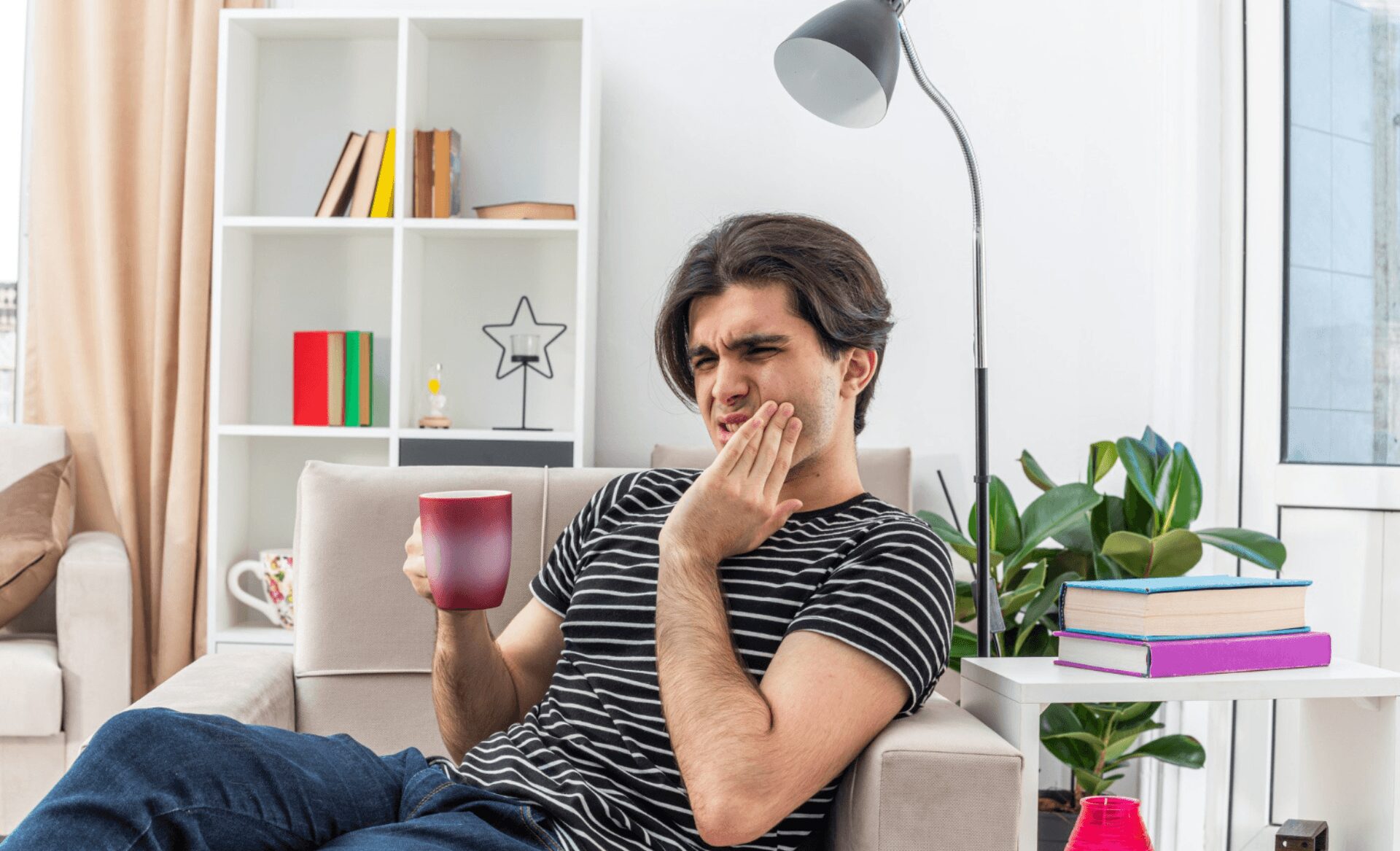 young man experiencing tooth pain at home while drinking coffee