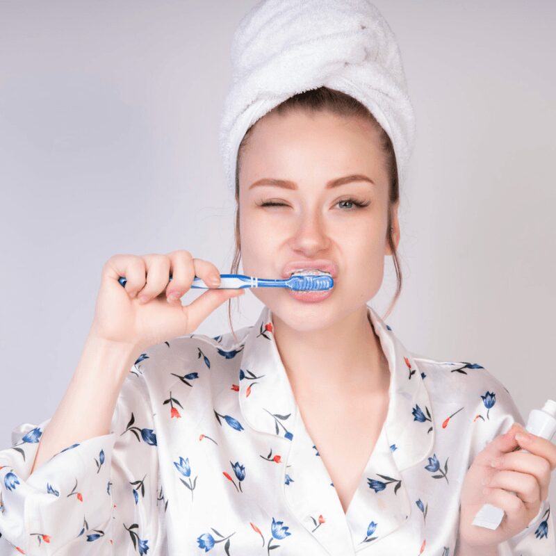 young girl brushing her teeth with blue tooth brush, holding tooth paste in her left hand